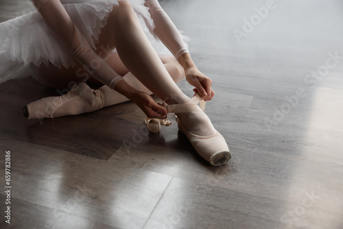 Ballerina sitting on floor putting on pointe shoes before choreography lesson