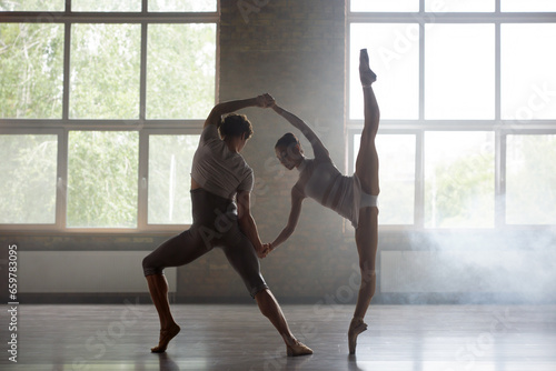 Man and woman ballet dancers performing together against studio background