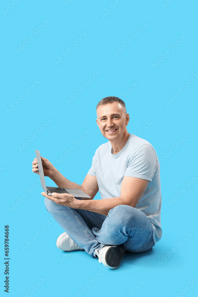 Mature male programmer with laptop sitting on blue background Mature male programmer with laptop sitting on blue background