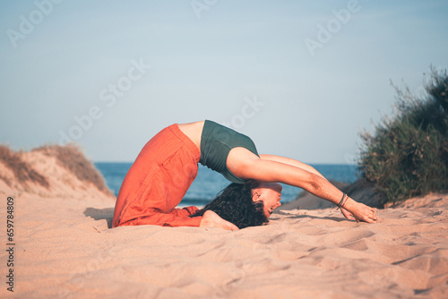 Flexible girl doing yoga pose on the sand of the beach