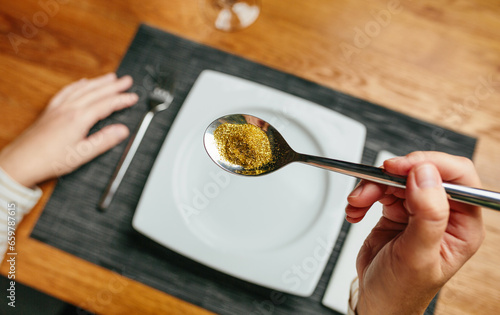 Unrecognizable woman hand holding a spoon full of golden glitter composed of plastics harmful to humans and environment. Concept about risks of eating food contaminated with microplastics.
