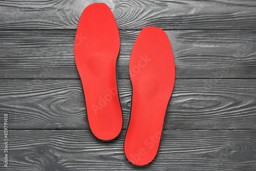 Pair of red orthopedic insoles on dark wooden background