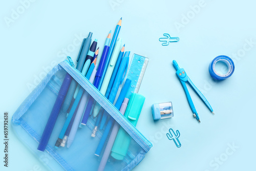 Stylish pencil case with different school stationery on blue background