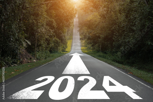 New year 2024 or straight forward concept. Text 2024 written on the road in the middle of asphalt road in the forest with sunrise. Concept of planning, goal, challenge, new year resolution..