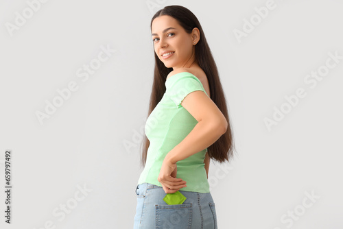 Young woman with condom in pocket on light background