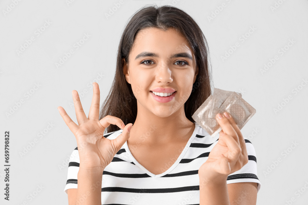 Young woman with condoms showing OK on light background. Birth control Young woman with condoms showing OK on light background. Birth control