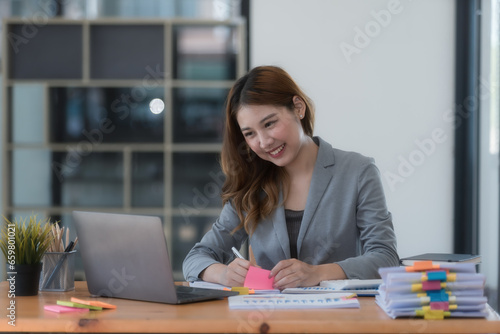 Portrait of smiling Asian businesswoman working on laptop at workplace in modern office.