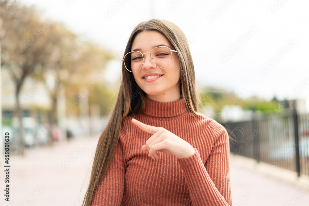 Teenager girl at outdoors With glasses and pointing side
