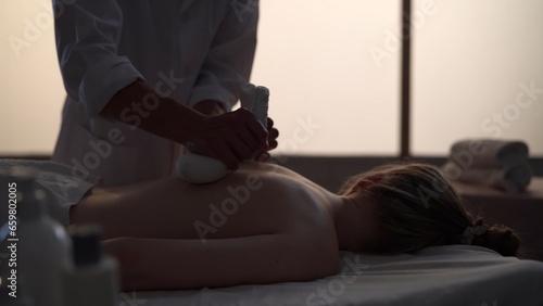 Medium shot. Masseur, massage specialist giving a massage to his patient using herbal bags. Silhouettes of a woman and a man in the massaging room, spa procedure.