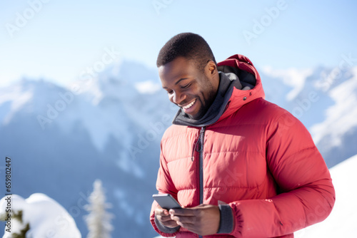 Happy african american man texting in smartphone in snowy mountains.
