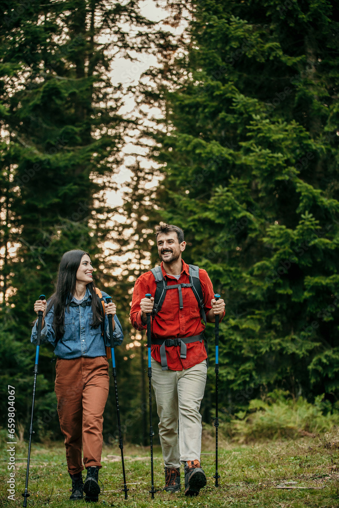 A couple with backpacks and walking sticks hiking in nature.