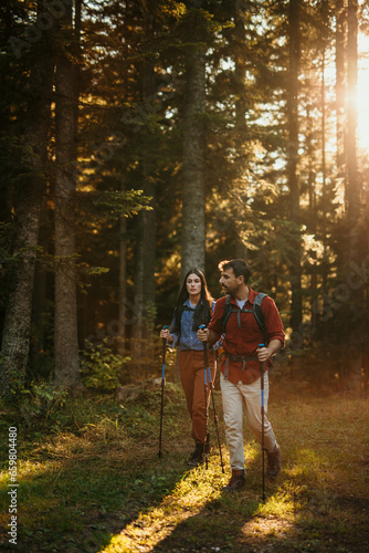 A multicultural pair with backpacks and walking sticks discover the beauty of the outdoors, their beaming smiles mirroring their excitement for the journey ahead