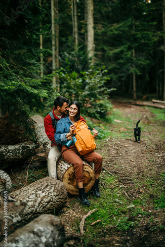 A multicultural couple, their backpacks leaning against the log, unwind and share a tender moment after conquering a rugged trail