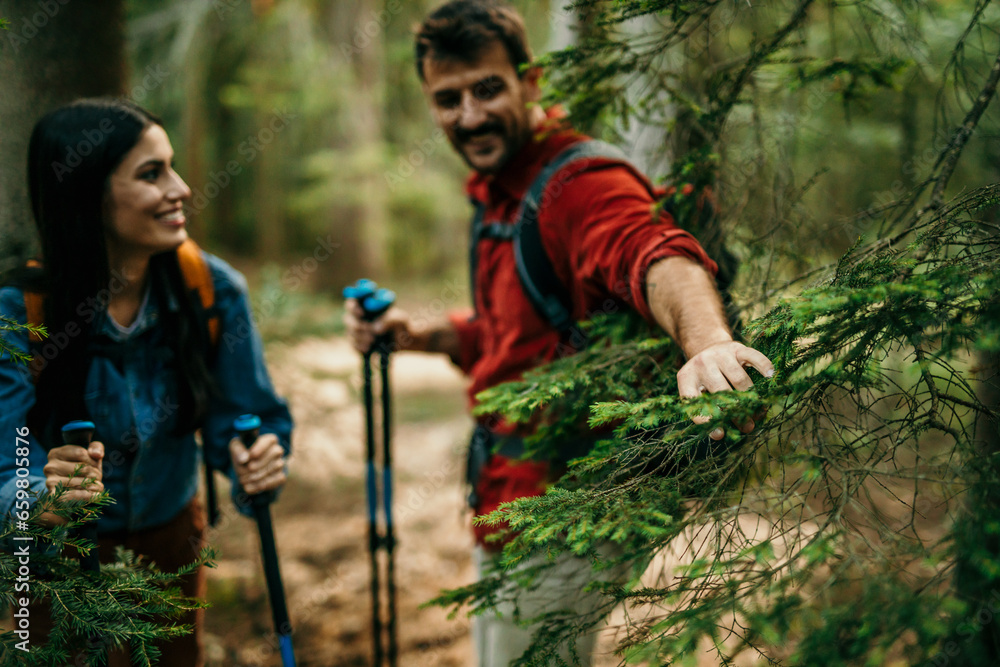 A multicultural pair, man clearing a way for a woman in the forest, their backpacks and trekking poles ready for the journey ahead A multicultural pair, man clearing a way for a woman in the forest, their backpacks and trekking poles ready for the journey ahead