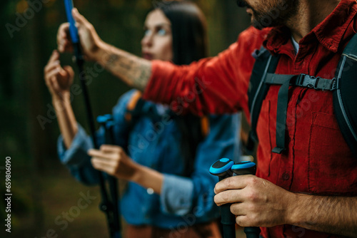 A multicultural pair, beaming with excitement, embarks on a scenic hike surrounded by lush greenery, their backpacks and trekking poles ready for the journey ahead