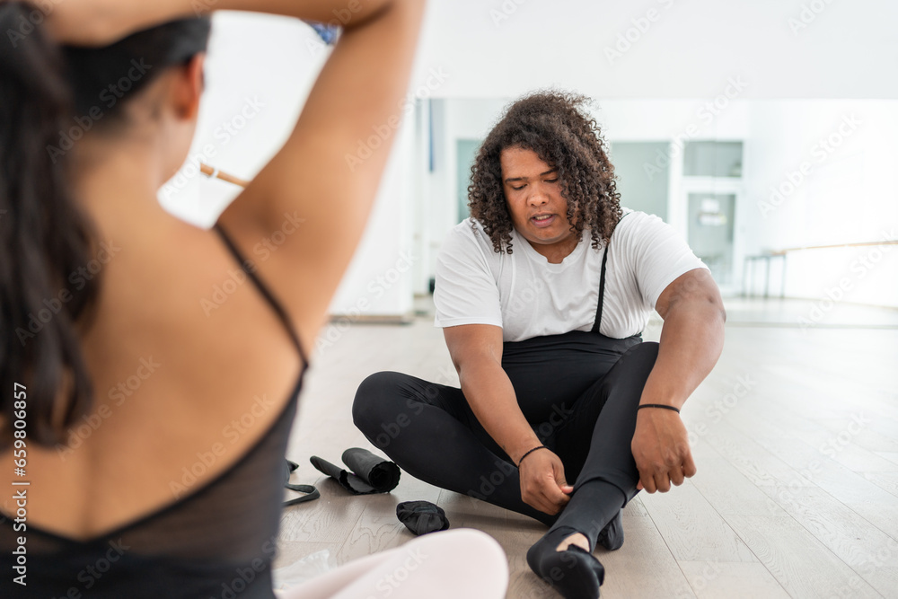 young male ballet dancers couple partners concentrated preparing before class; african american man getting ready putting on dance shoes and leotard young male ballet dancers couple partners concentrated preparing before class; african american man getting ready putting on dance shoes and leotard