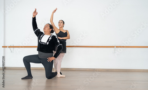 multiethnic dance partners performing an act in a dance studio in front of a big mirror; hispanic ballerina dancing with an african american plus sized young man