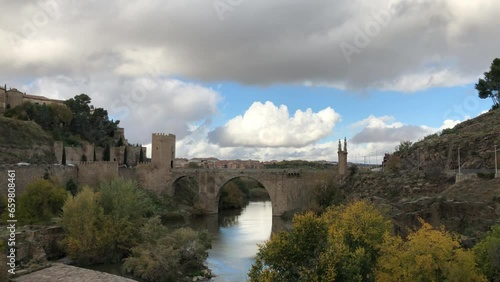 Shot of Alcantara Bridge over Tagus river, reflecting white cotton clouds and blue sky. Roman & medieval style arch bridge, Toledo, Spain. Slow atmosphere. photo