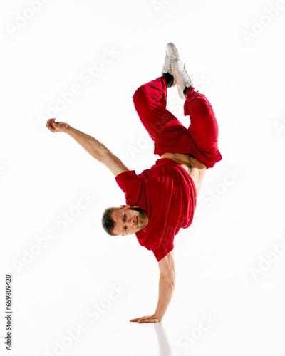 Young attractive man, guy, dancer wearing stylishly cloth dancing hip-hop, breakdance elements, freezes against white background.