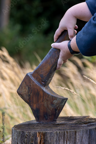 Close-up of a woman holding a wooden ax in her hand on a tree stump in autumn