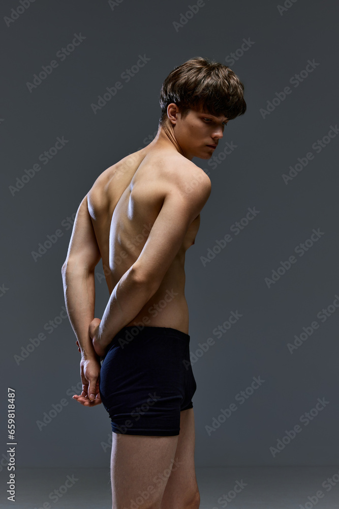 Rear view portrait of muscular shirtless young man posing like antique sculpture in underwear against grey studio background. Masculinity. Rear view portrait of muscular shirtless young man posing like antique sculpture in underwear against grey studio background. Masculinity.