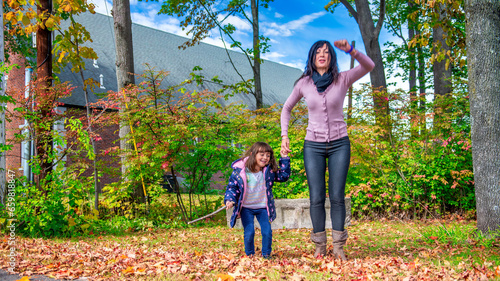 A happy young girl jumping with her mother in the forest, autumn foliage season