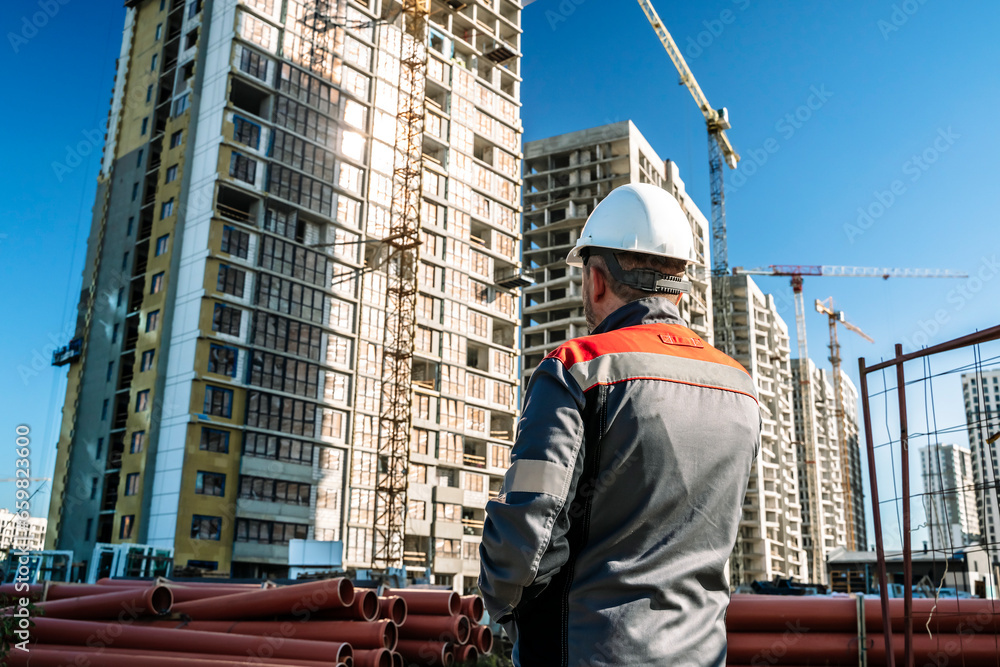 Builder at a construction site. Construction of a high-rise building and a builder looking at the process Builder at a construction site. Construction of a high-rise building and a builder looking at the process