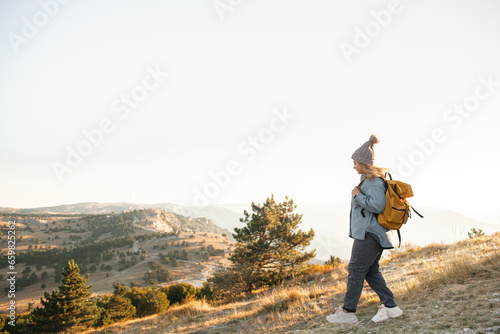 The plus size woman walks in the mountain. The gil admires beautiful views of landscape. Travel and tourism. Hiking. The overweight woman holding yellow bagpack