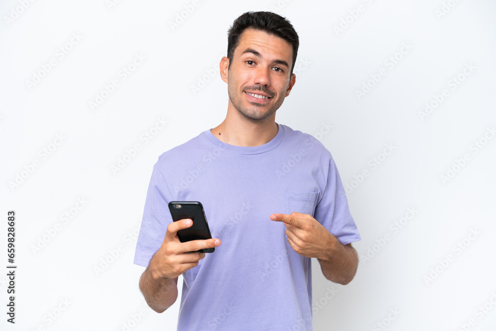 Young handsome man over isolated white background using mobile phone and pointing it Young handsome man over isolated white background using mobile phone and pointing it