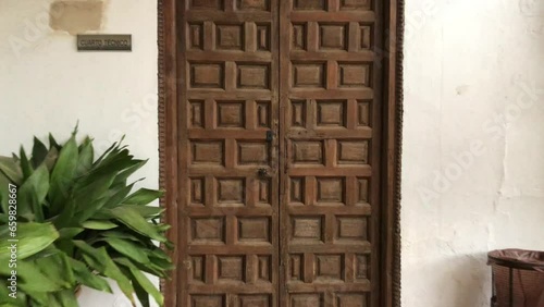 Dolly out shot of an Islamic style wooden door with a square chocolate shape on a white Alhambra wall on a rainy day in Granada, Spain.