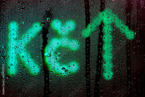 Blurred glowing Czech koruna sign with arrow up made from light bulbs.The symbol of the national currency behind a rain-wet window with water drops in the night.Sign of economic rise.