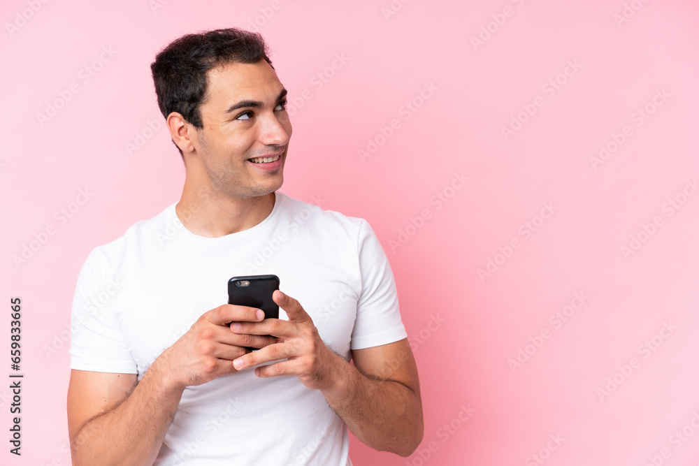 Young caucasian man isolated on pink background using mobile phone and looking up Young caucasian man isolated on pink background using mobile phone and looking up