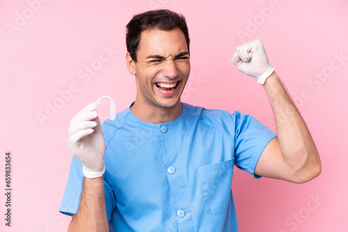 Dentist caucasian man holding invisible braces isolated on pink background celebrating a victory