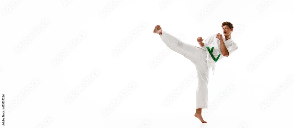 Young man, karate, taekwondo athlete in kimono and green belt training isolated on white studio background. Concept of martial arts, combat sport, energy, strength, health. Banner. Copy space for ad