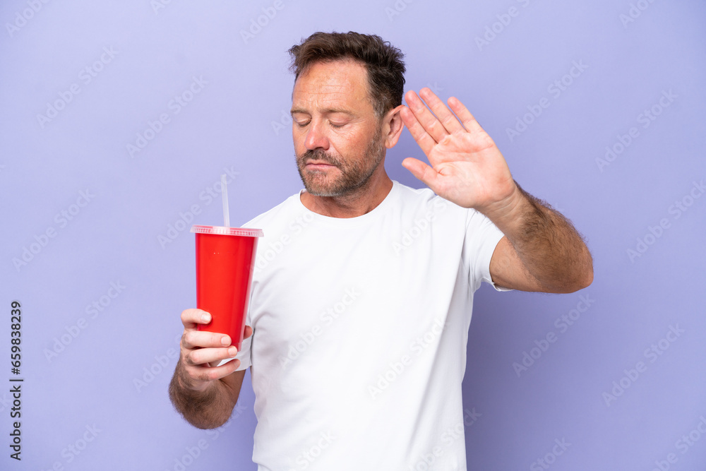 Middle age caucasian man holding soda isolated on purple background making stop gesture and disappointed Middle age caucasian man holding soda isolated on purple background making stop gesture and disappointed