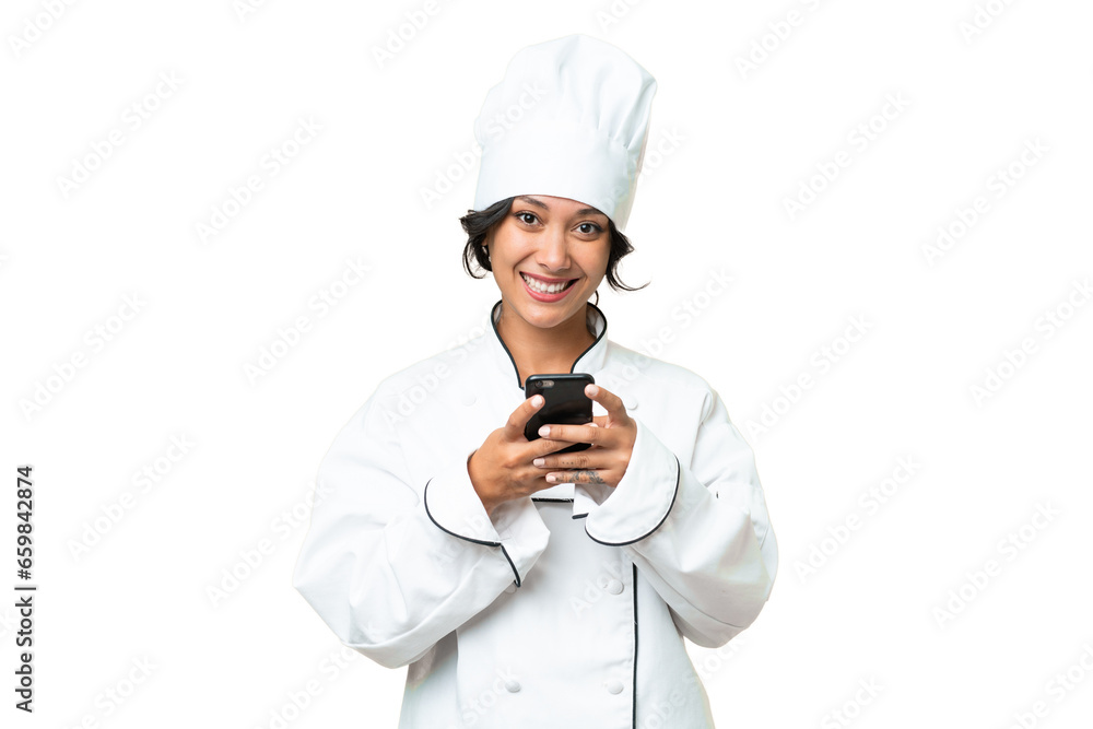 Young chef Argentinian woman over isolated background sending a message with the mobile Young chef Argentinian woman over isolated background sending a message with the mobile