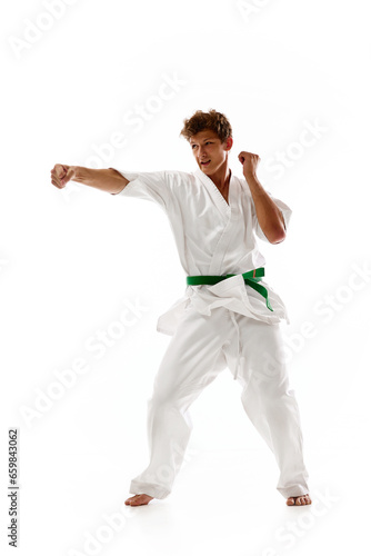 Young man, karate, judo, taekwondo athlete in motion, training, fighting isolated on white studio background. Concept of martial arts, combat sport, energy, strength, health. Ad