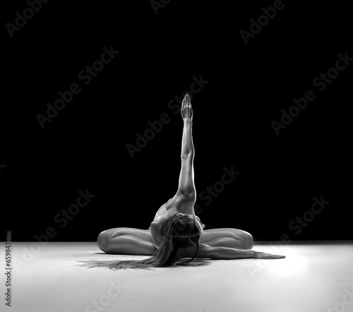 Beautiful nude sexy fitness girl with a great muscular figure flexing her perfect body in a yoga pose at the strange studio. Black and white photo.