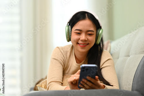 Cheerful young woman in headphone chatting with friends in social media on smartphone