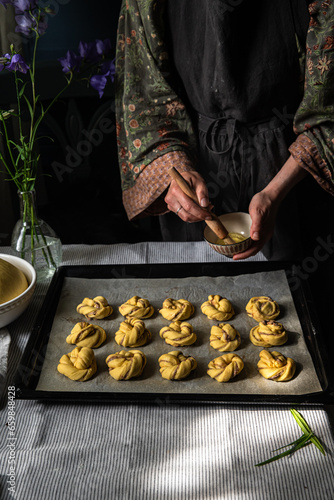 Step by step process of making traditional Swedish cinnamon buns. Woman brushing cinnamon buns with egg whites.