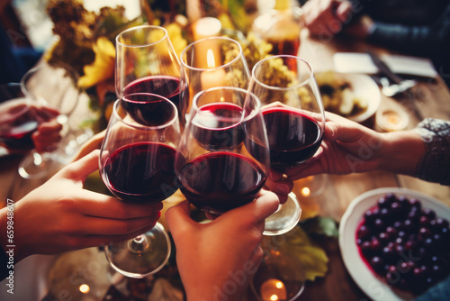 People clinking with a glasses filled with red wine sitting at the Thanksgiving dinner table