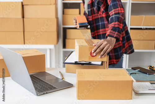 Beautiful Asian startup owner at home with laptop and package boxes in SME supply chain, omnichannel purchasing or online sales idea. Close-up pictures