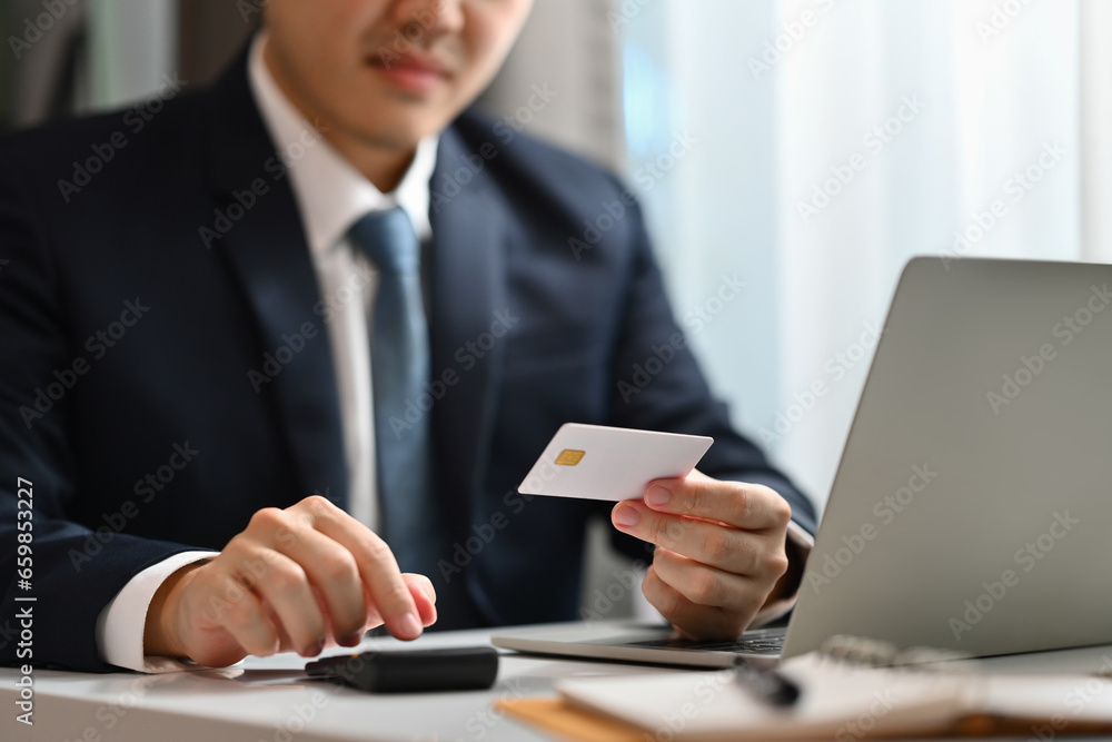 Businessman hand holding credit card and using laptop. E-commerce, online shopping, internet banking concept Businessman hand holding credit card and using laptop. E-commerce, online shopping, internet banking concept