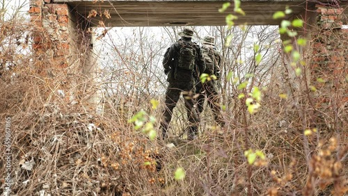 The silhouette of two soldiers in camouflage uniforms with weapons among the dry grass.  photo