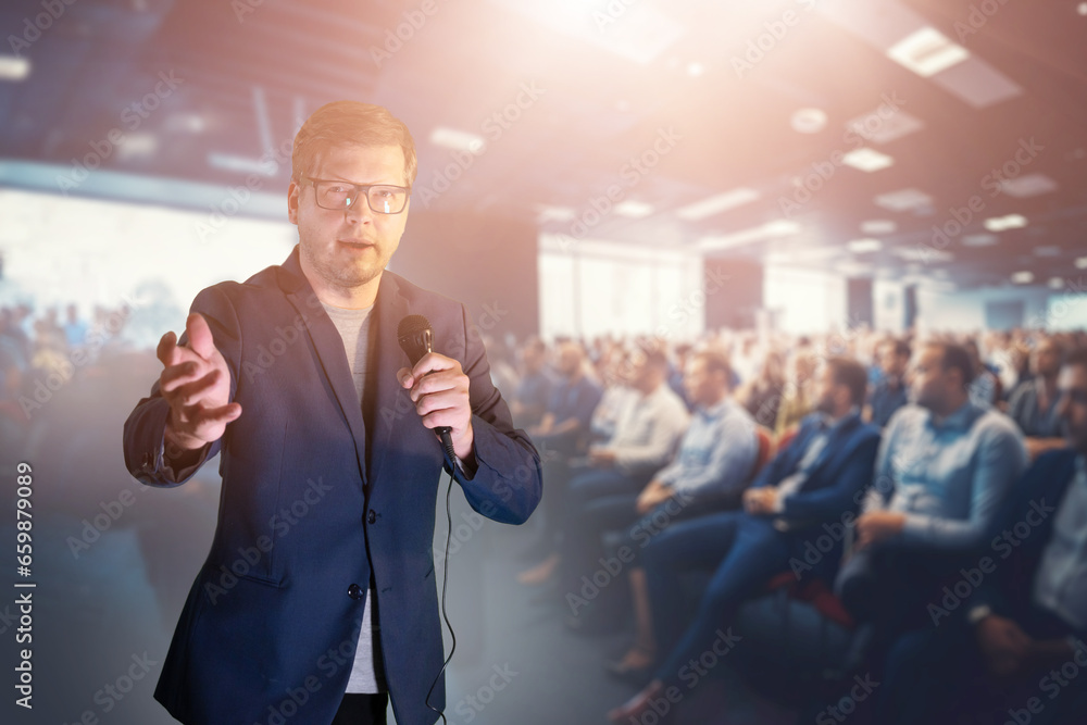 a businessman man talks to the audience into a microphone at a business seminar a businessman man talks to the audience into a microphone at a business seminar
