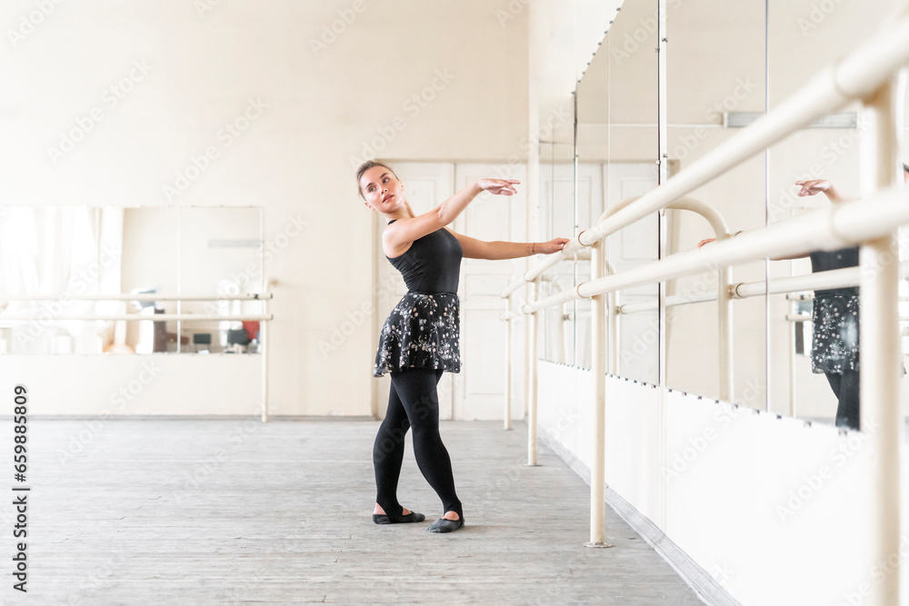 young woman doing ballet dance practice, standing near ballet rail in
