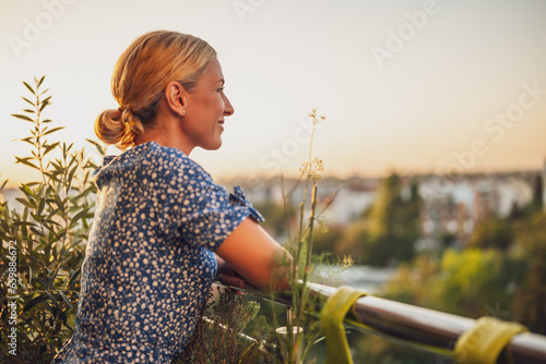 Fotografia Beautiful woman enjoys standing on her balcony at sunset.