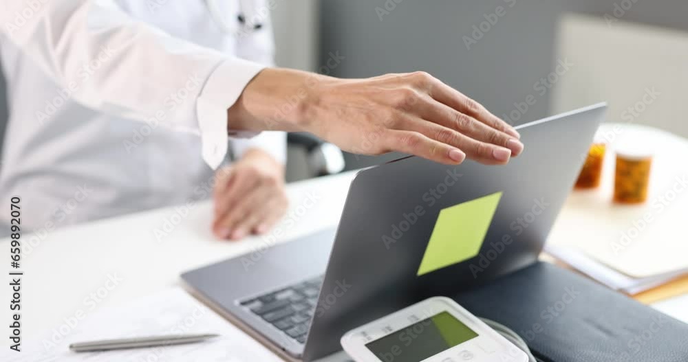Doctor opens laptop while sitting at workplace. Medical working day concept Doctor opens laptop while sitting at workplace. Medical working day concept