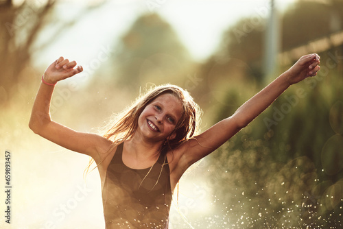 In the backyard of house, a young girl bursts with laughter and joy as she gleefully runs through a water sprinkler on a sunny summer day