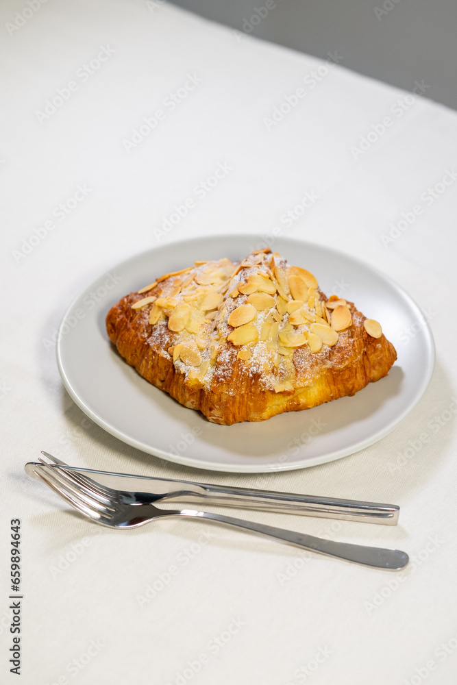 Croissants with almonds and powdered sugar are served on a plate.